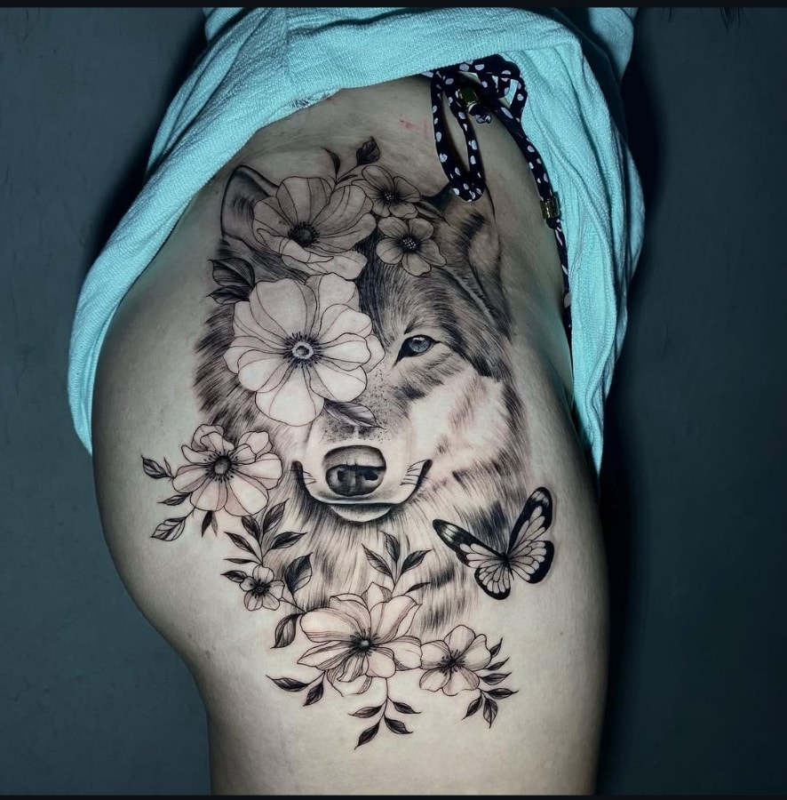 Tatuagem de lobo com flores e borboleta na coxa